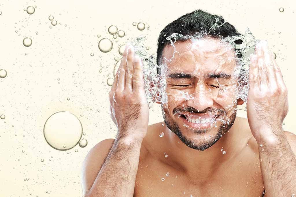 A happy man washing his face, representing skincare for men.